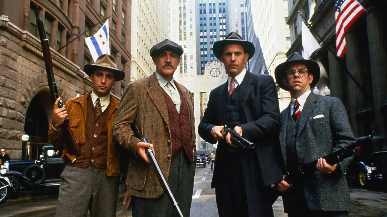 Four men in hats and 1920s garb hold shotguns and look at camera