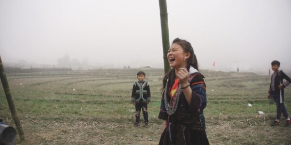 A young girl stands in a misty field and laughs joyously, with two younger boys in the background
