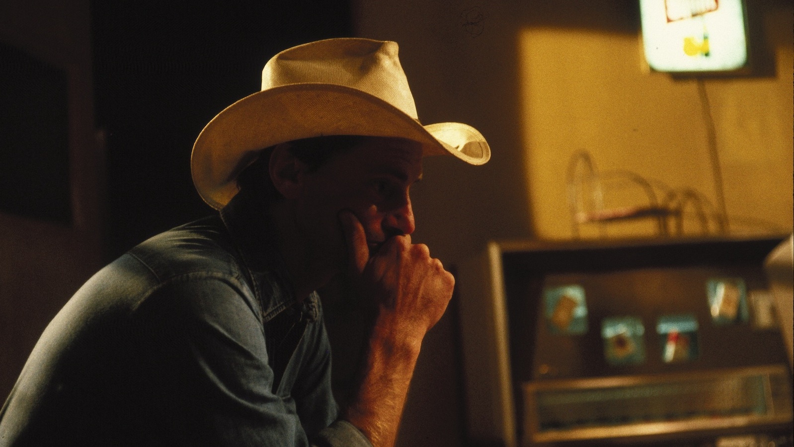 A man in shadow in a motel room wearing a stetson in profile