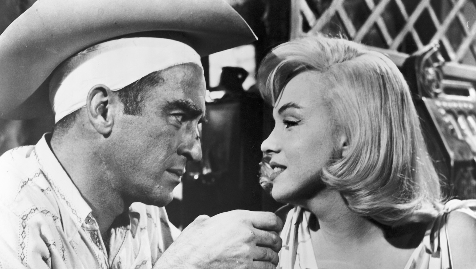 Black and white shot of a man and woman looking at each other in close up. He wears a cowboy hat