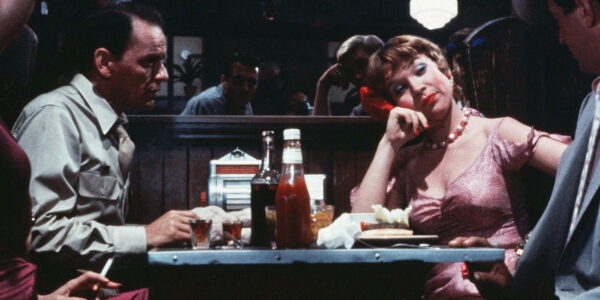 A man and woman in a diner at a table with a bottle of ketchup between them. He looks at her, she looks away.