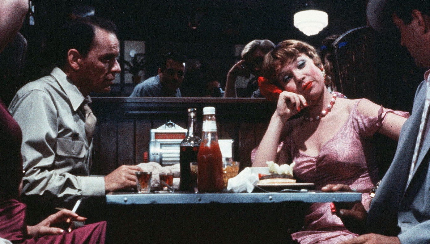 A man and woman in a diner at a table with a bottle of ketchup between them. He looks at her, she looks away.