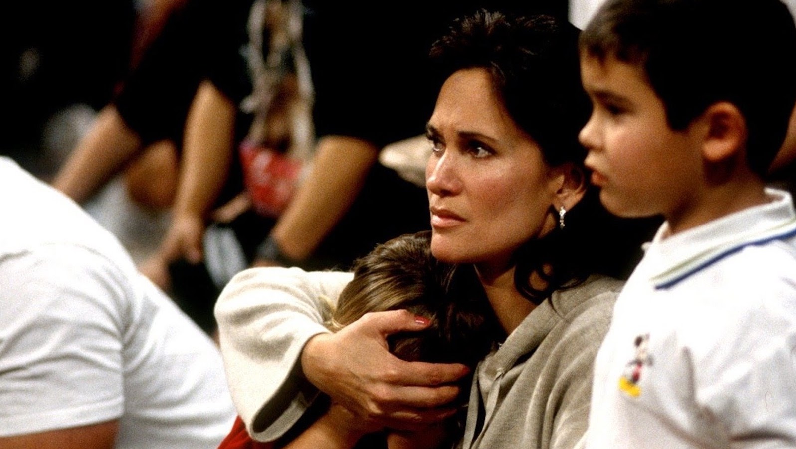 A woman in a sporting arena looks concerned as she holds her child's head close to her and another child stands beside her