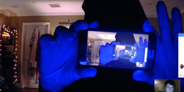 A hooded figure holds a cell phone that shows the same image over and over in a hall of mirrors