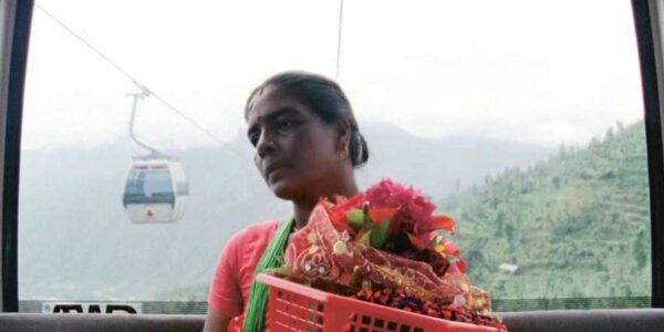 A woman carries a red basket full of flowers in a gondola high in the mountains