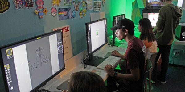 A young man in a hat sits staring at computer screen with a green light on the wall behind him
