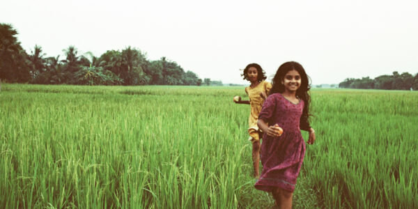 two young girls run through verdant green tall grasses towards the camera