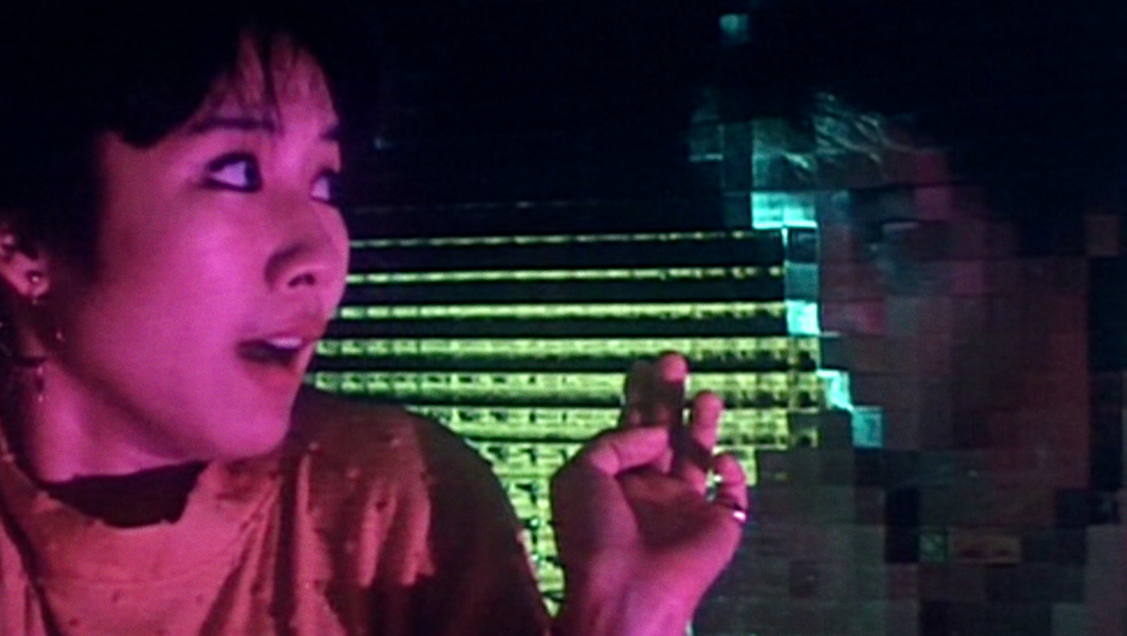 A woman bathed in purple light recoils in terror from a face behind a distorting glass window staring at her