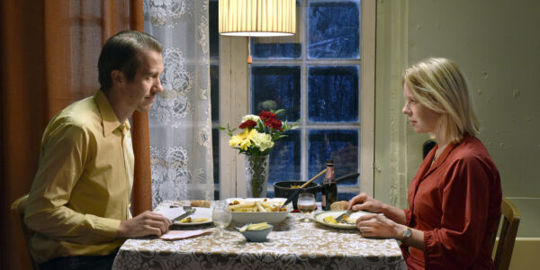 A man and woman sit at a table with flowers on it having dinner and facing each other