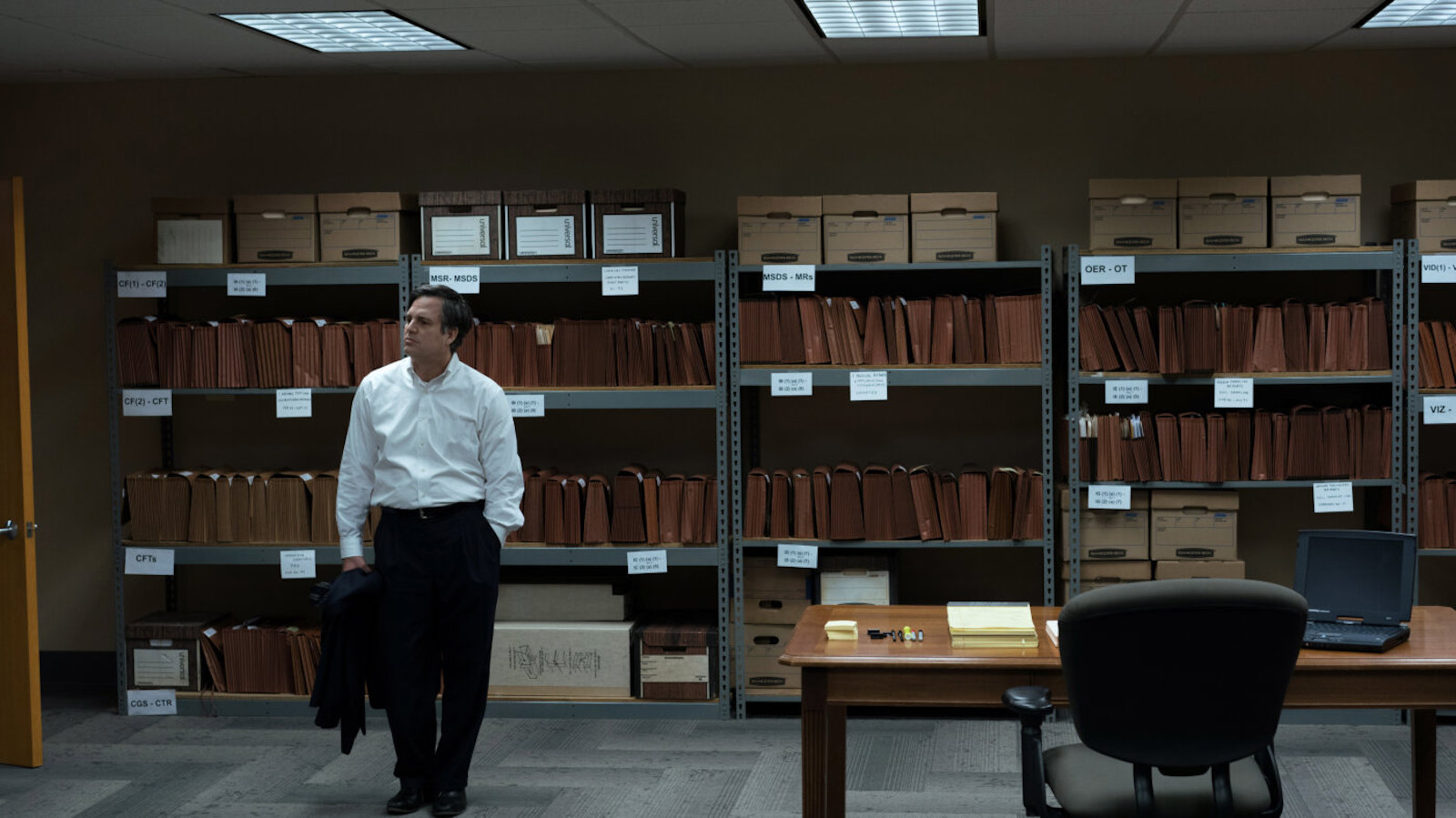 A man in a white dress shirt stands in a warehouse full of file folders
