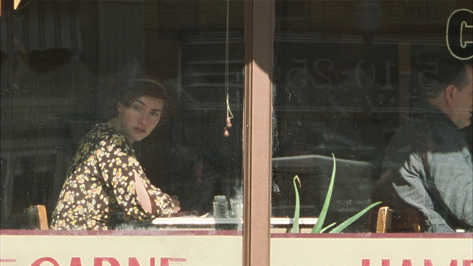 A woman in 1930s dress sits in the window of a diner looking out