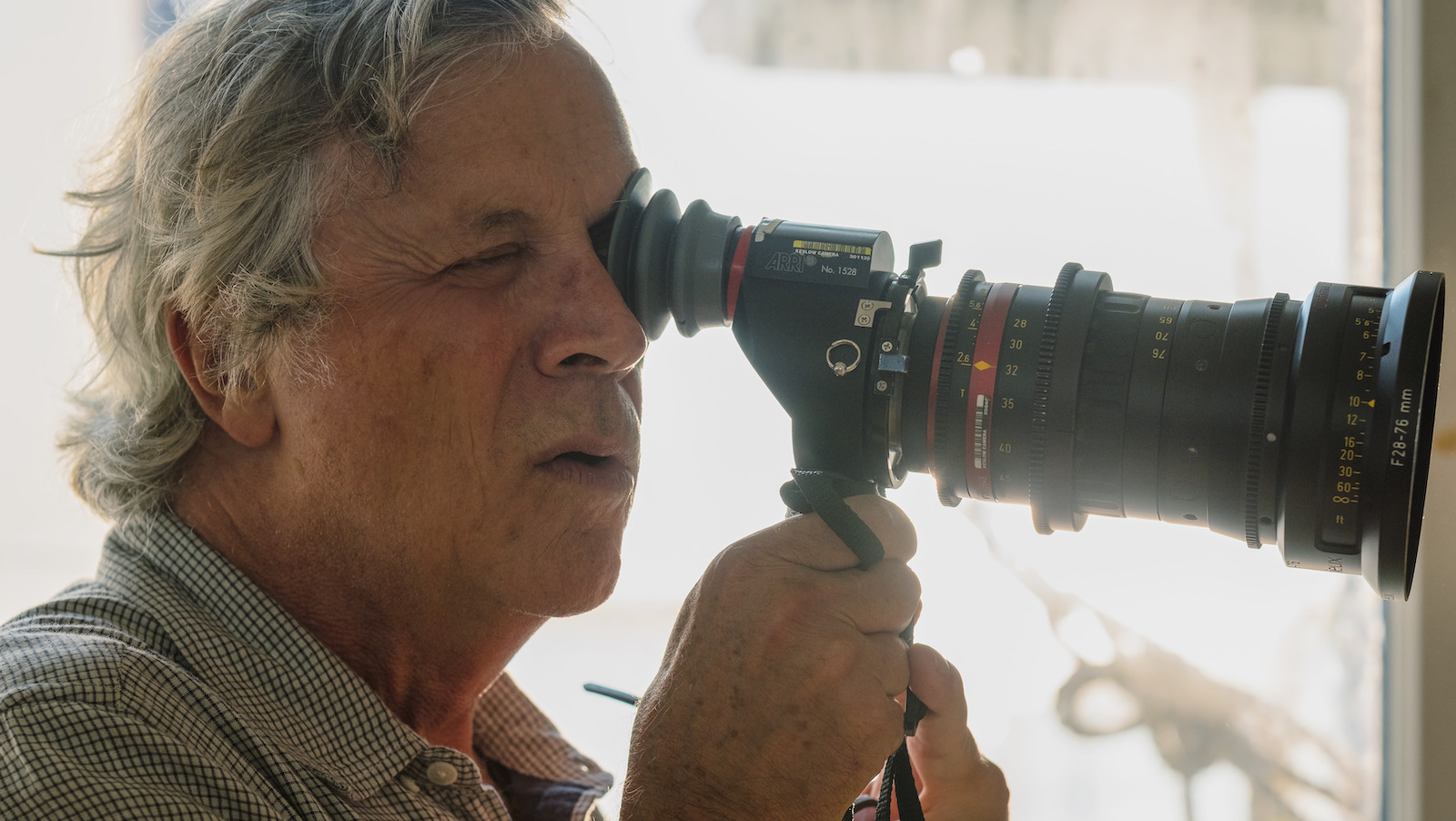 A man in profile looks through a camera viewfinder
