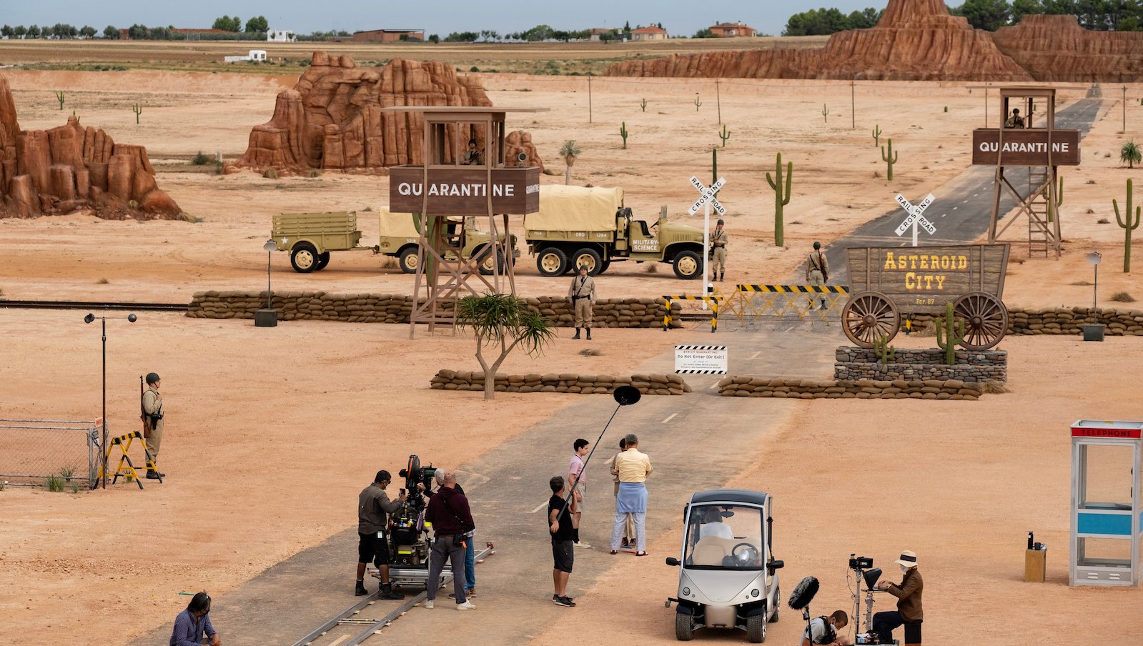 A beige western city surrounded by desert with a film crew standing around.