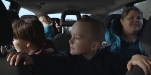 A child sits in the backseat of a car, gripping the headrests of the front seats.