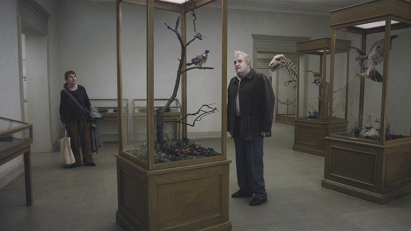 A man with pale ghostly makeup stands looking at models of birds at a museum