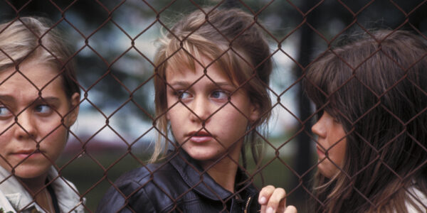 Three girls look through a chain link fence