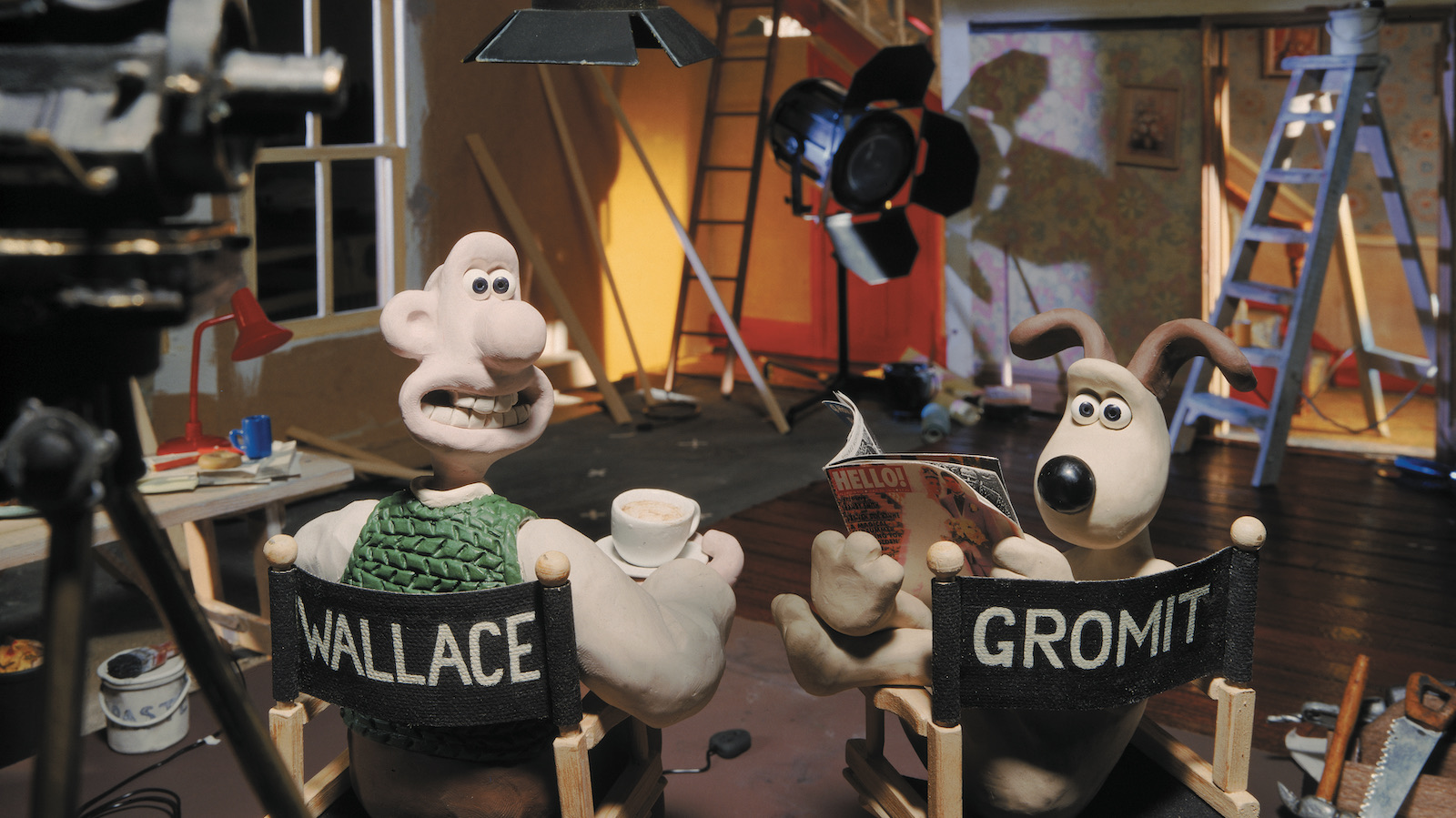 A claymation image of a man and his dog sitting on director's chairs, turning their heads back towards the camera