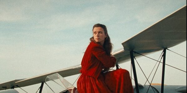 A woman dressed all in red sits on the top of a biplane