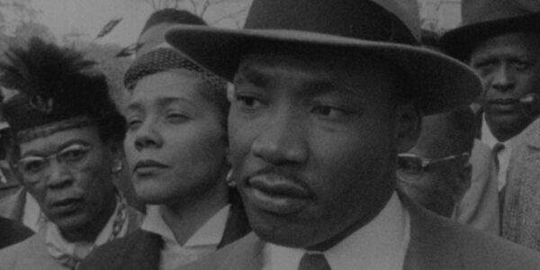 Martin Luther King Jr stands in a crowd wearing a fedora