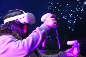 A young woman wearing a virtual reality headset and holding a controller, bathed in purple light