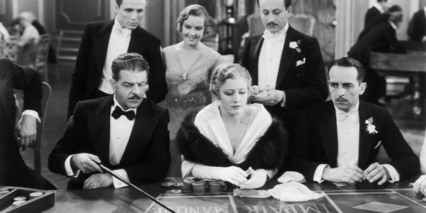 A woman sits at a casino table surrounded by men in a black and white image