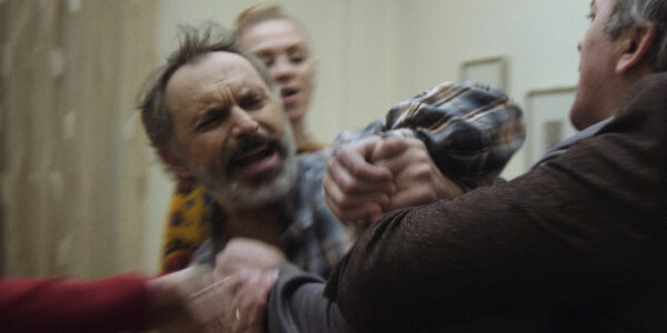 A white-bearded man struggling with another man during a fight inside a house