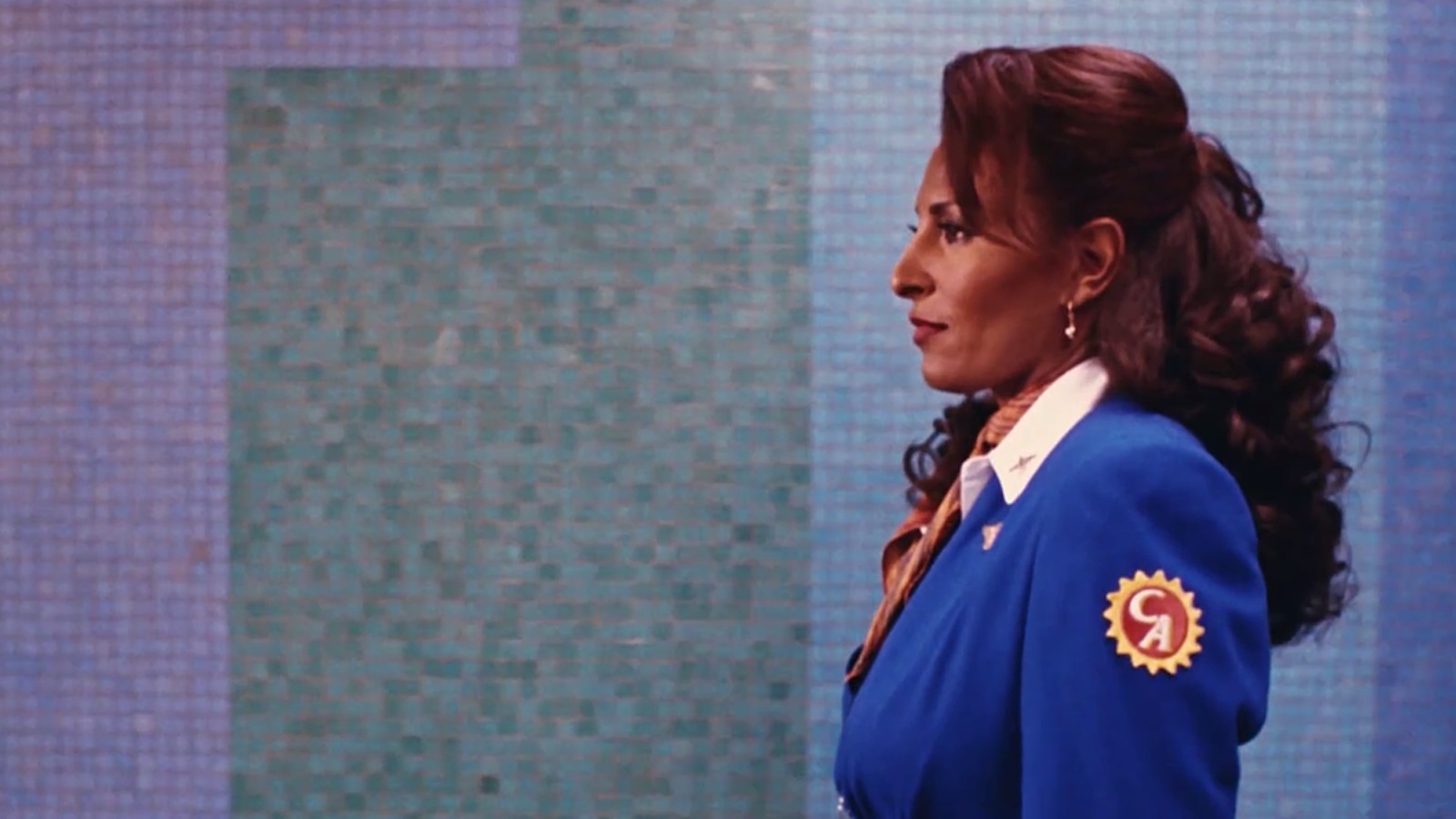 A woman in an airline attendant blue suit in profile against a colorful tiled wall at an airport