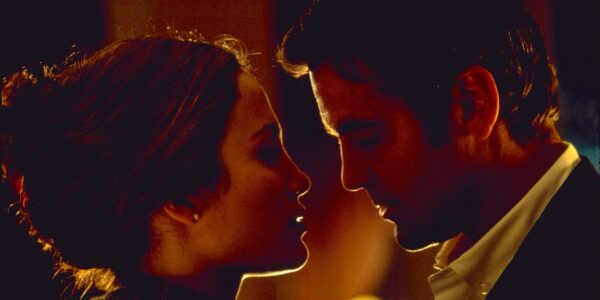 A close up of a man and woman looking at each other in a dark room in profile, ready to kiss