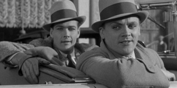 Two gangsters in fedoras sneer from a car in a black and white image