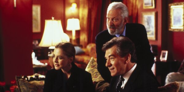 Three people, two men and a woman, lean forward expectantly, on a couch as they look at someone off screen.