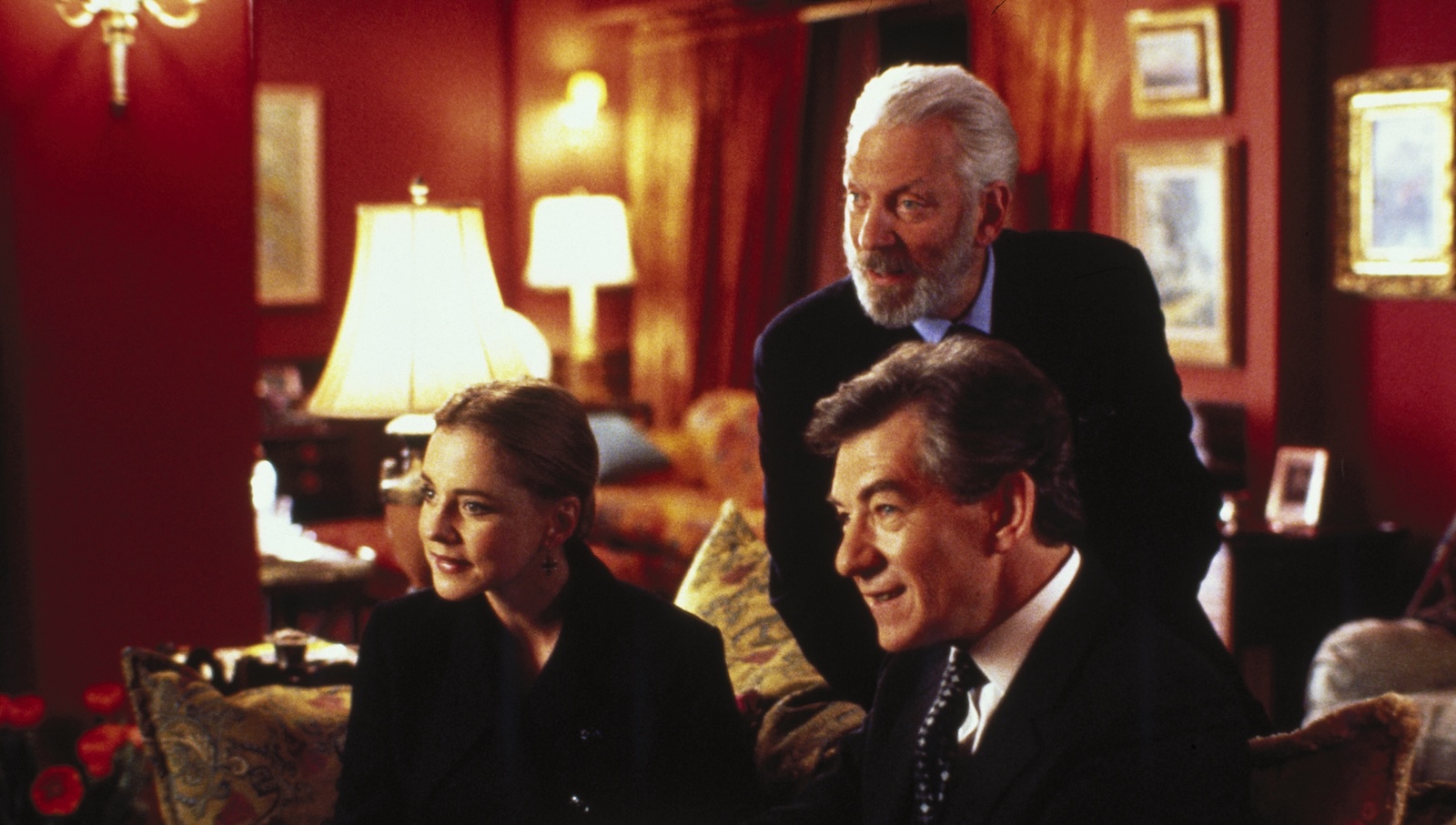 Three people, two men and a woman, lean forward expectantly, on a couch as they look at someone off screen.
