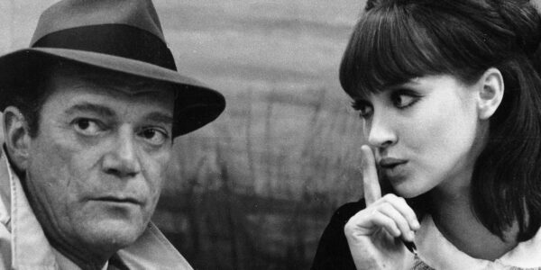 A black and white image of a man in a fedora sits next to a woman putting her finger to her lips in a "be quiet" expression.