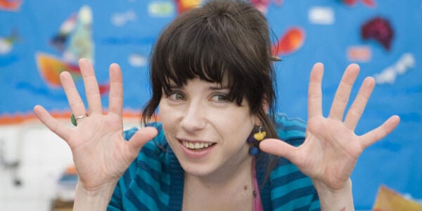 A smiling woman raises her hands and splays out her fingers in front of a blue painted wall