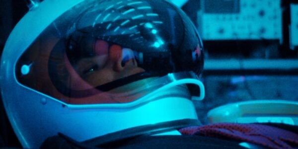 A man in a space helmet reclines, with reflections of lights on the glass viser