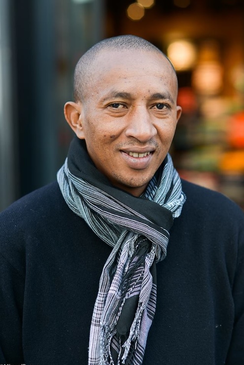 A man in a gray scarf smiles to camera