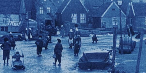 A blue-tinted image of a village in the Netherlands from the turn of the 20th century, with people walking across an icy street