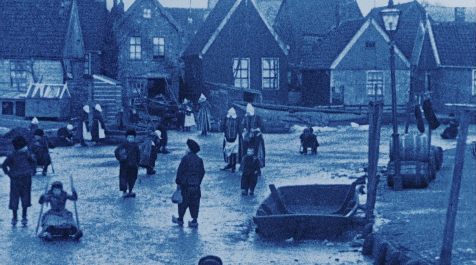 A blue-tinted image of a village in the Netherlands from the turn of the 20th century, with people walking across an icy street