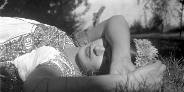 A woman lies in the grass, her arm covering her eyes.