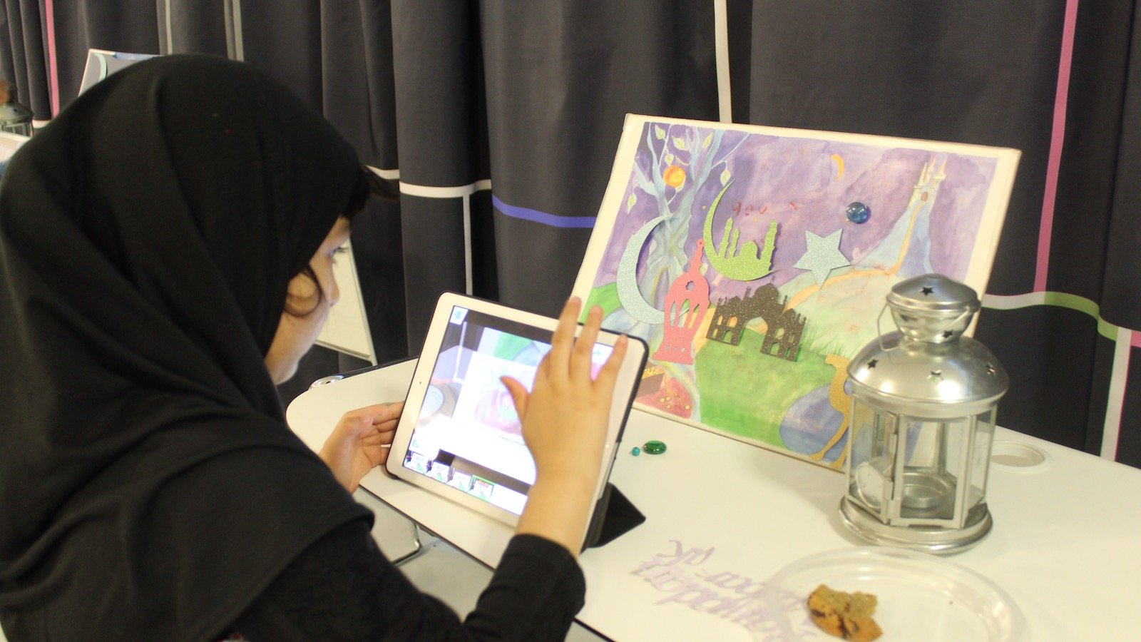A young girl in a hijab touches the screen of an iPad making animations