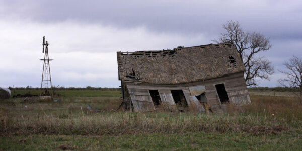A dilapidated barn leans over in a vast green field