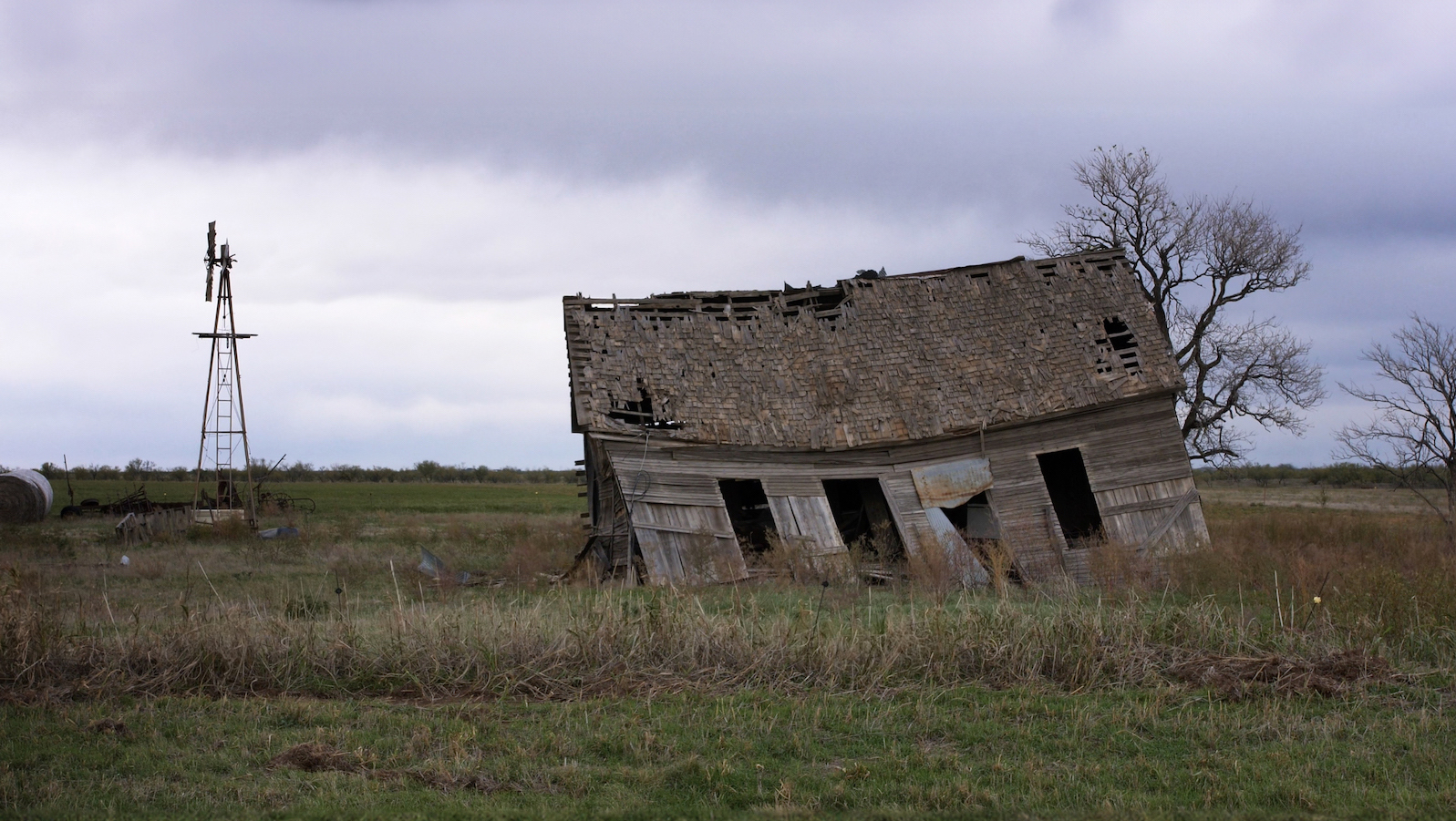 A dilapidated barn leans over in a vast green field