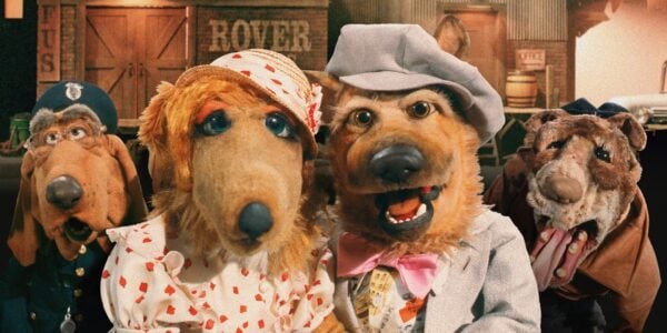 Four puppet dogs dressed in human clothes and hats look at the camera, smiling.