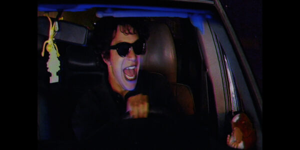 Person in sunglasses screams with mouth open while driving a car at night