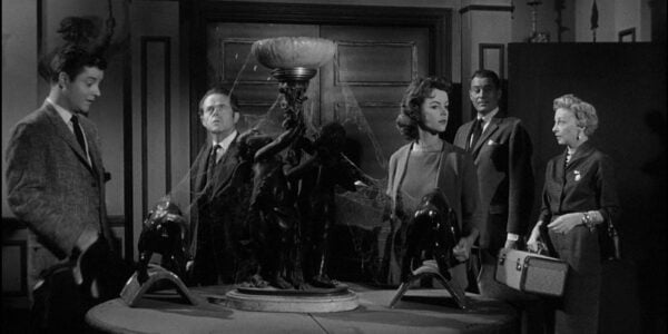 Five people stand in a dark room in an old house with cobwebs in a black and white image