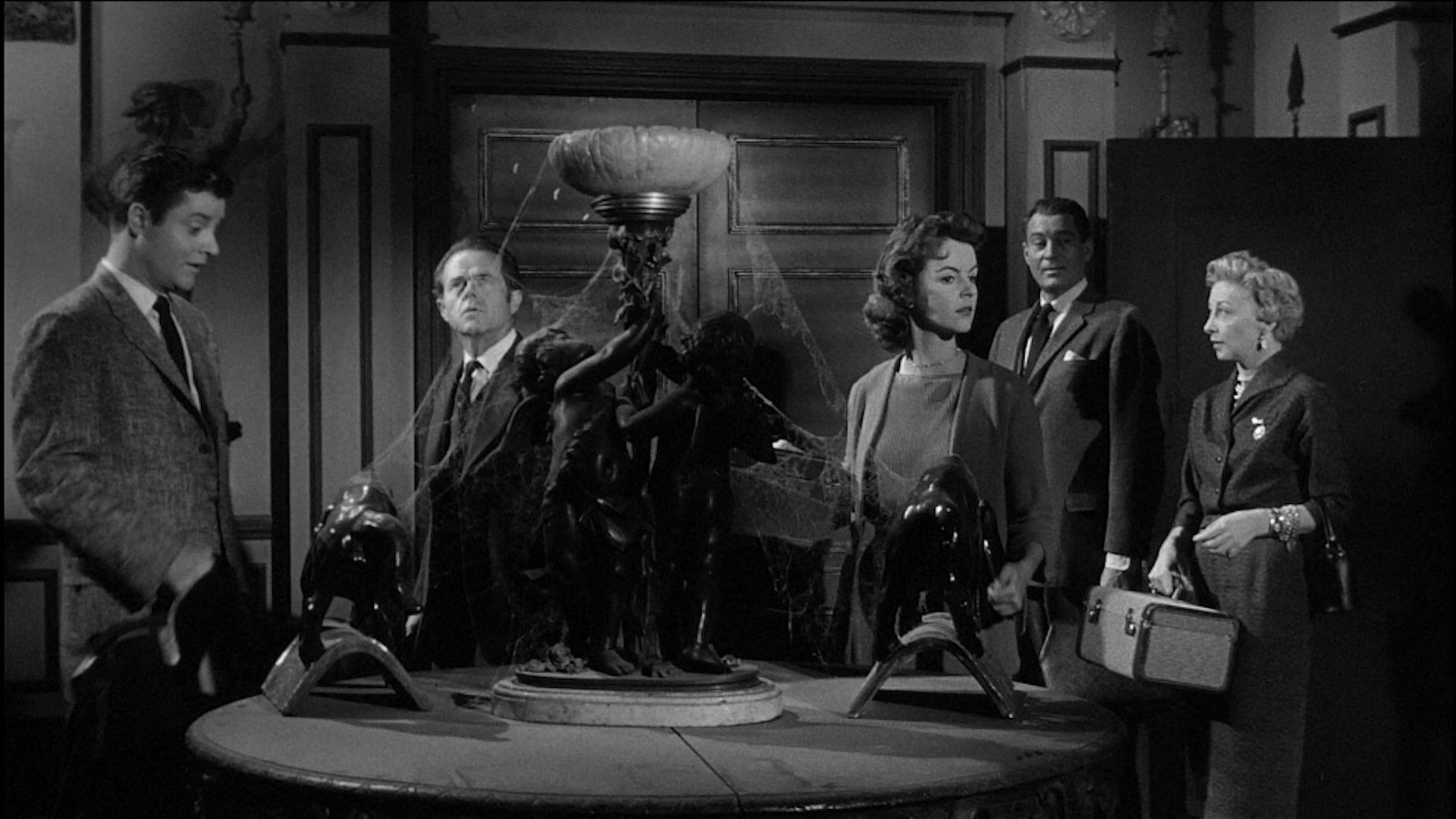 Five people stand in a dark room in an old house with cobwebs in a black and white image