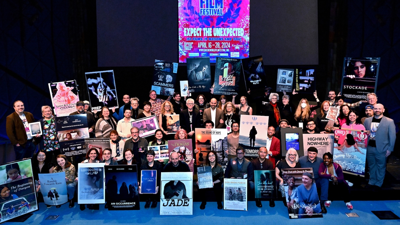 A large group of people in a movie theater posing for the camera while holding up a variety of movie posters