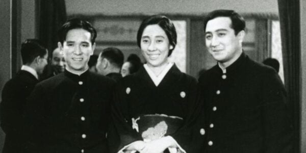 Black and white photo of three Japanese people in uniforms, a woman in the middle and two men on either side, smiling past the camera