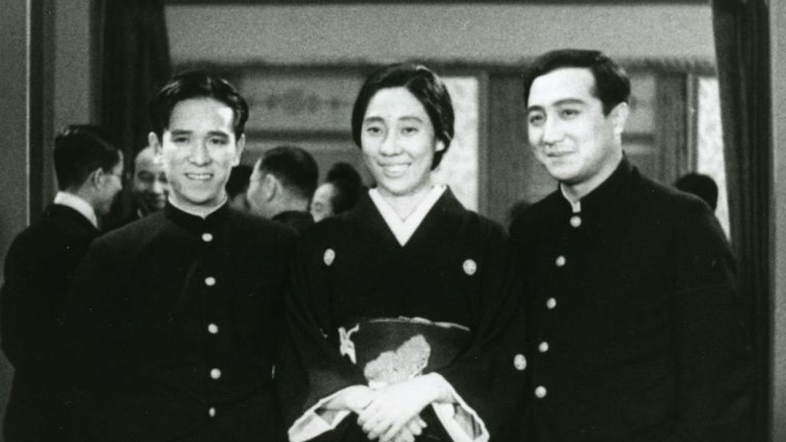 Black and white photo of three Japanese people in uniforms, a woman in the middle and two men on either side, smiling past the camera