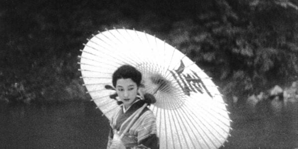 A black and white photo of a woman in classical Japanese clothing holding an elaborate parasol.