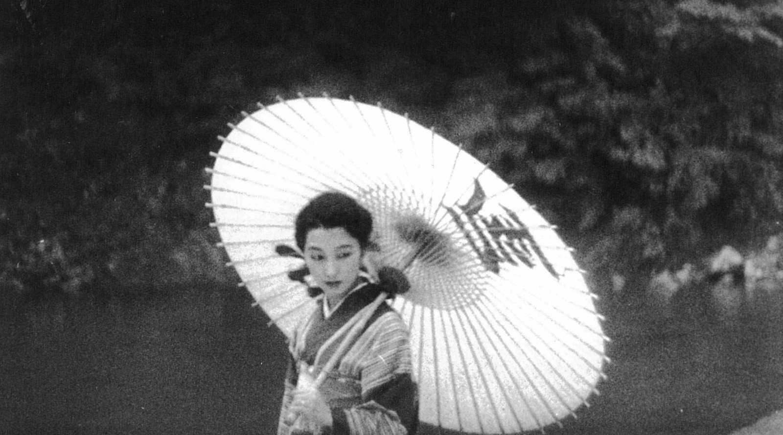 A black and white photo of a woman in classical Japanese clothing holding an elaborate parasol.